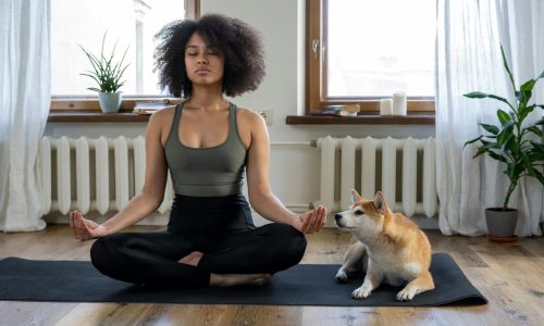 Mulher negra meditando sentada no chão proximo de um cachorro.